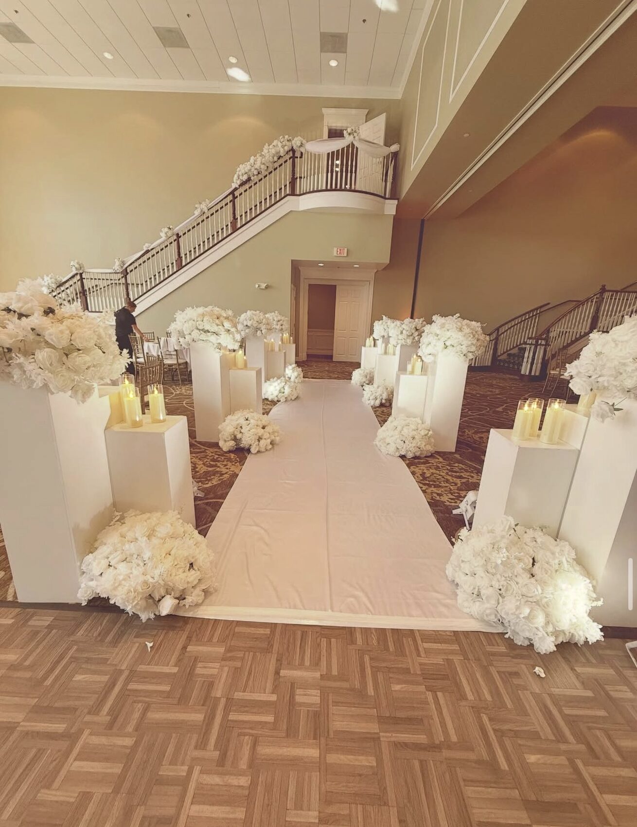 Foyer aisle lined with white floral pedestals and candles by a grand staircase