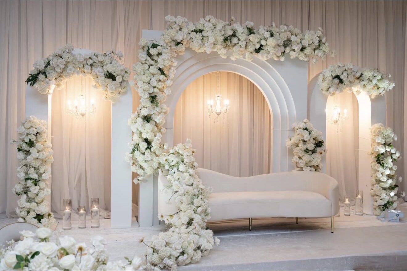 Luxury wedding stage styling with arched floral backdrops, chandeliers, and an elegant cream sofa