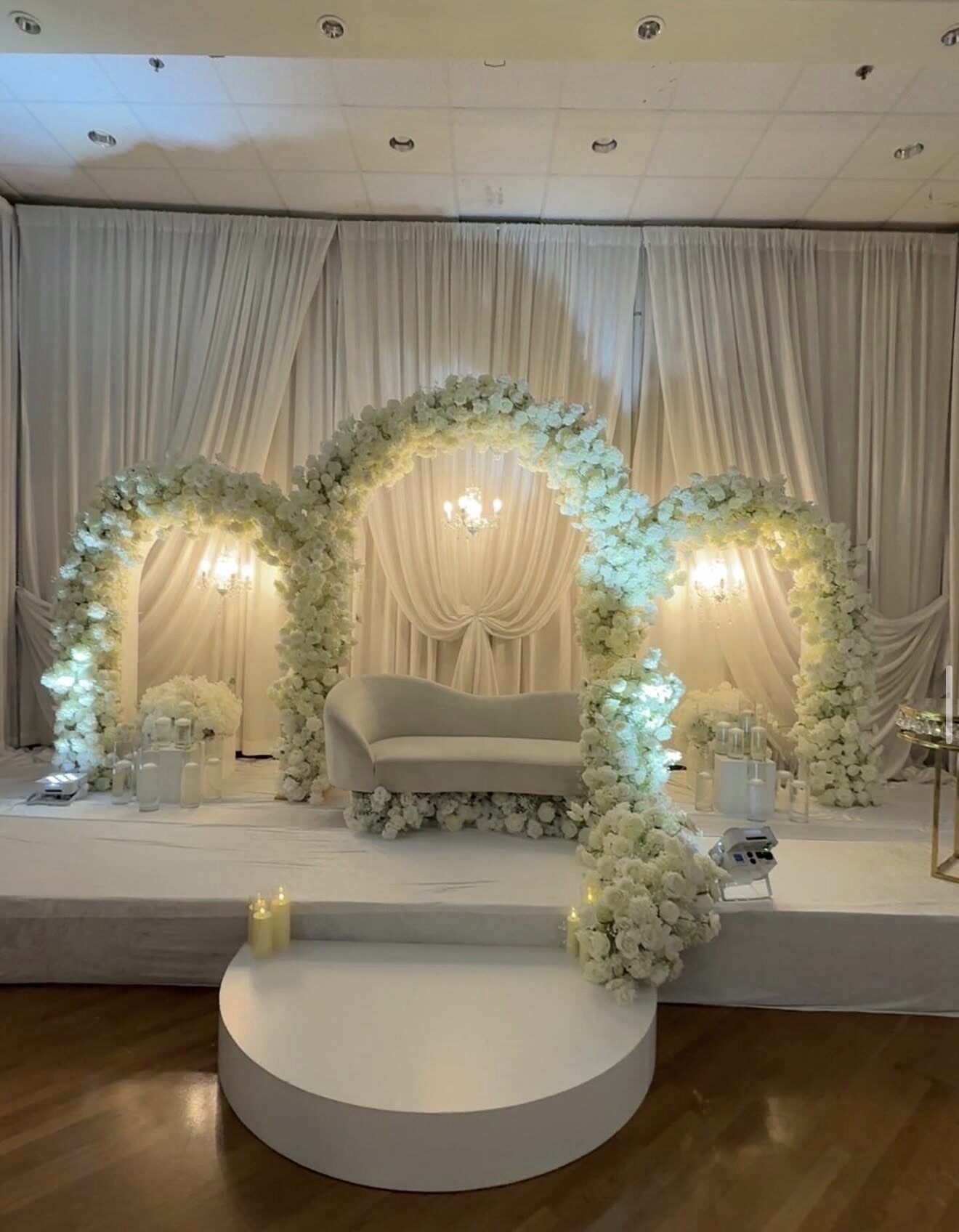 White floral moon arch framing an elegant cream sofa under warm chandelier light